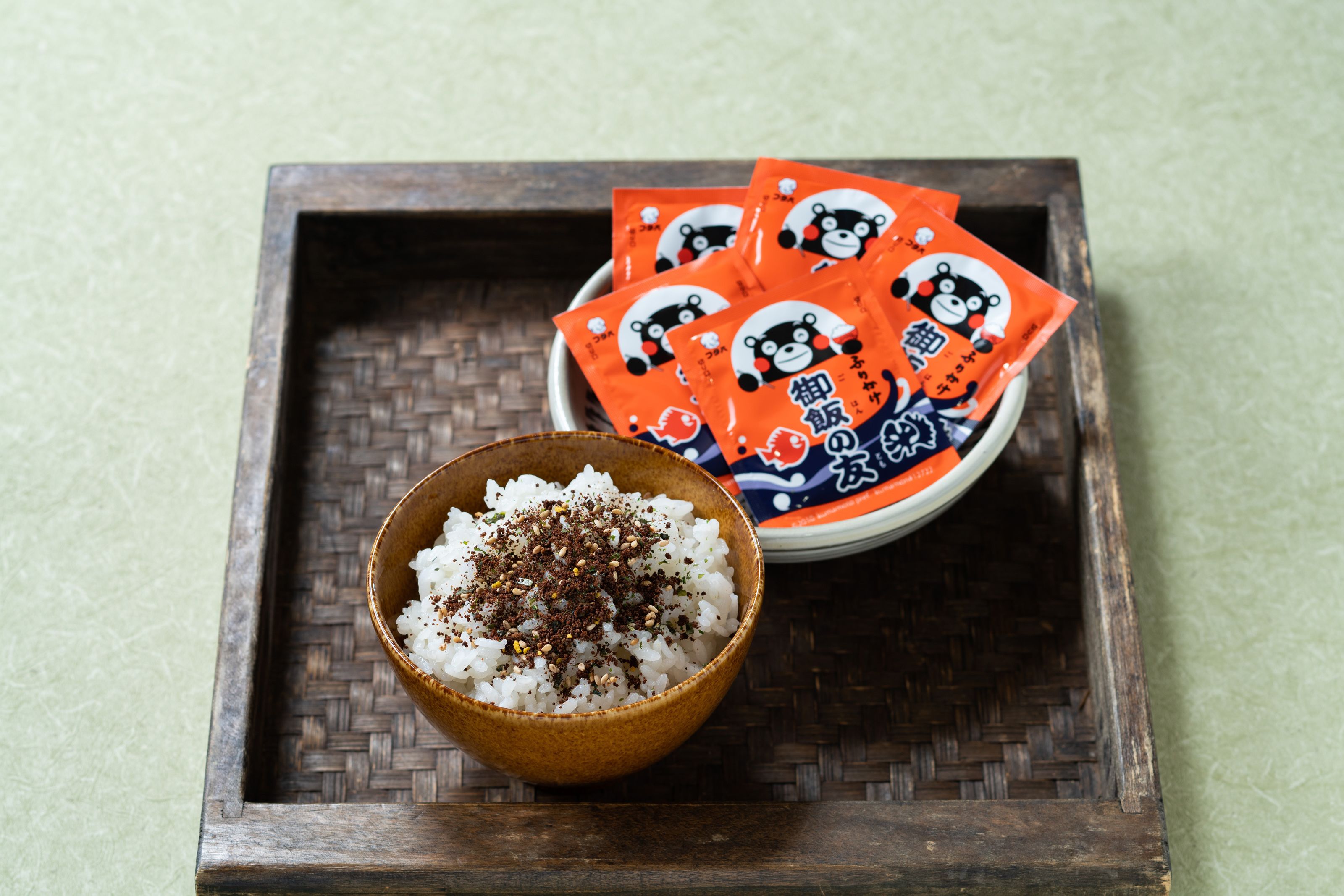 A wooden tray with a bowl of rice and packets of snacks.