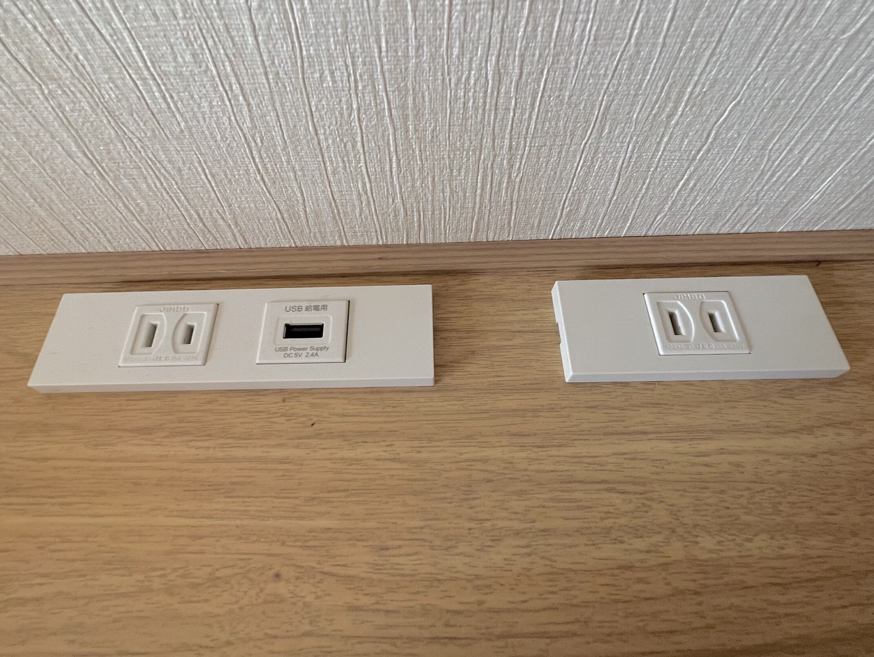 Dues preses de corrent murals sobre una superfície de fusta, una amb alimentació USB.