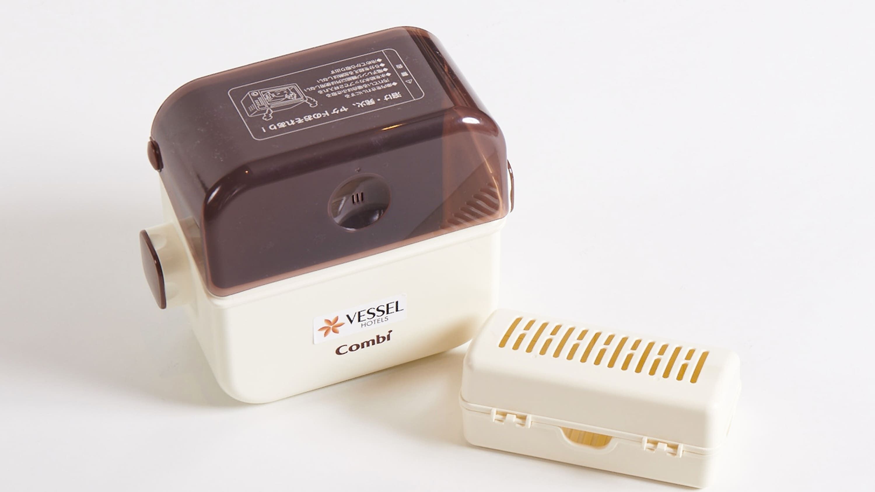 A compact, two-part device with a brown top and a white base, featuring the VESSEL HOTELS logo and the word "Cambi" on the base.