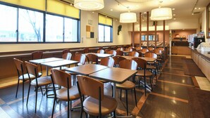 Een restaurant met houten tafels en stoelen, grote ramen en een keukenhoek.