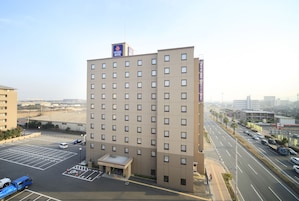 A multi-story hotel with a flat facade, a parking lot, and a street view.