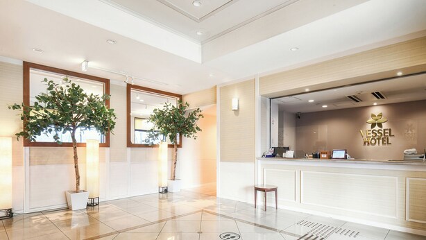 Een receptiehal van een hotel met een modern ontwerp, inclusief een receptiebalie, twee potplanten en een grote spiegel.