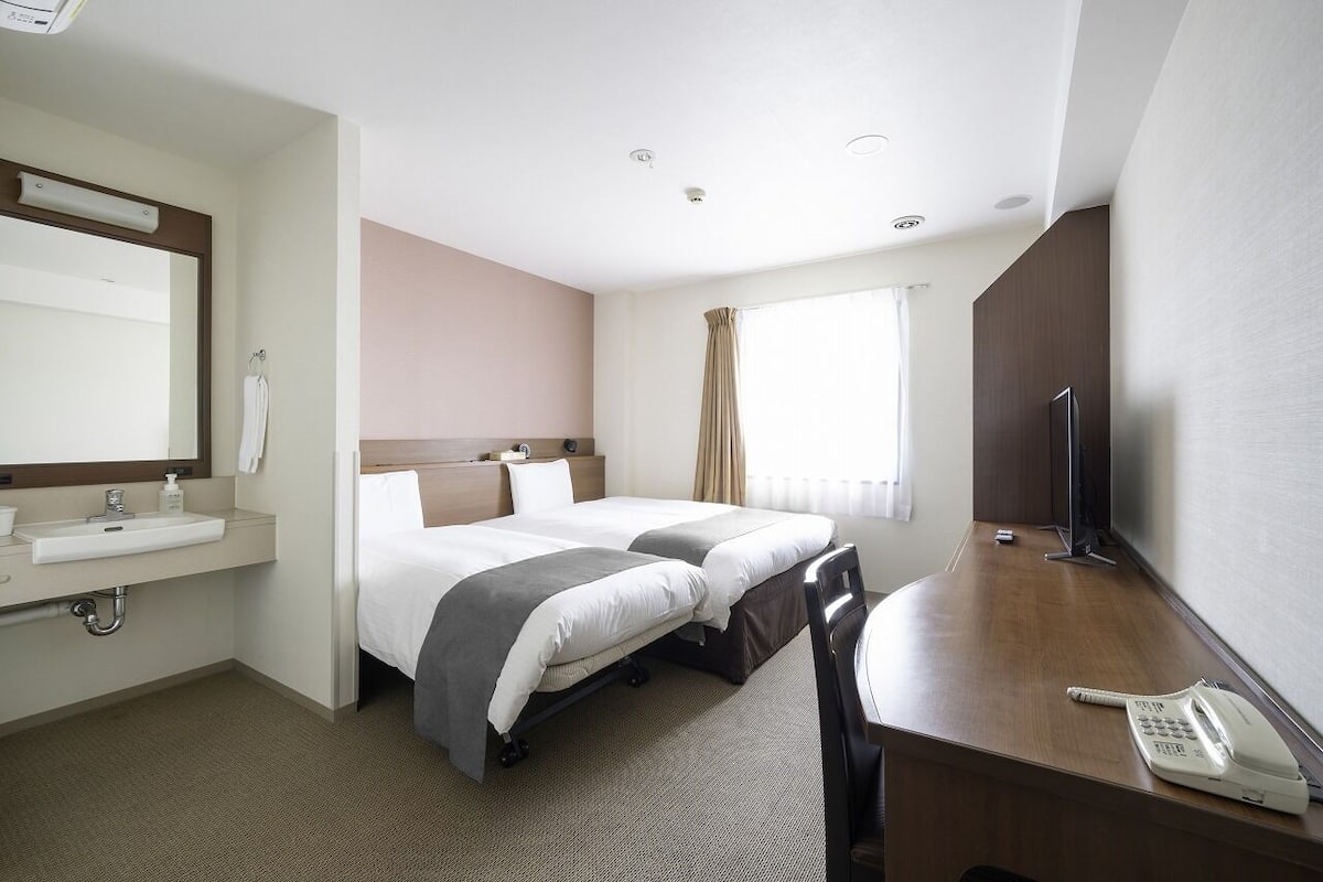 Ett hotellrum med en säng, ett nattduksbord, ett skrivbord, en stol och en telefon.