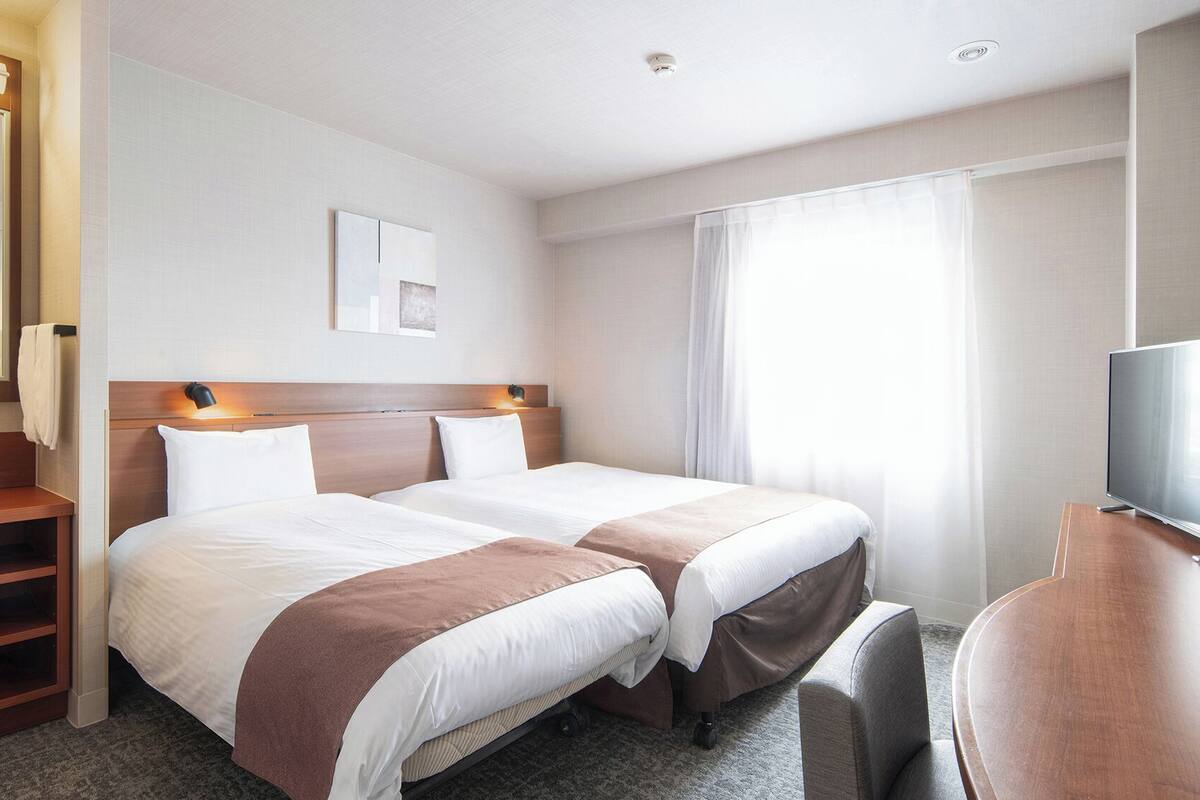 Ett hotellrum med två sängar, ett skrivbord, en tv och ett badrum med spegel och handfat.