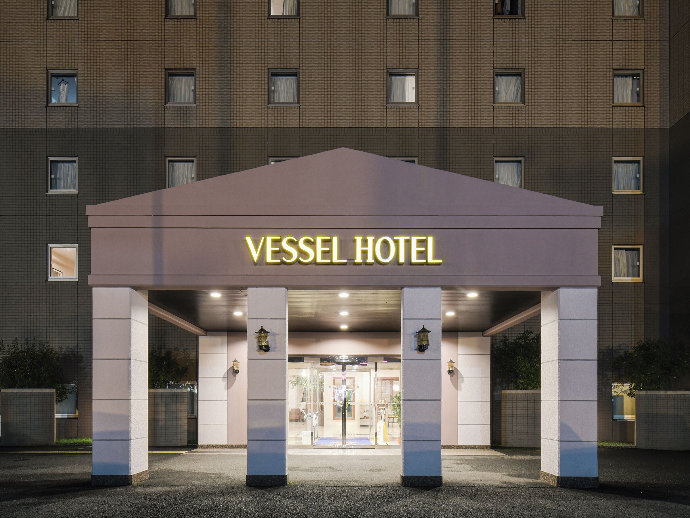 La entrada del Hotel Vessel, con un diseño moderno, presenta un letrero destacado y un área de acceso cubierta.