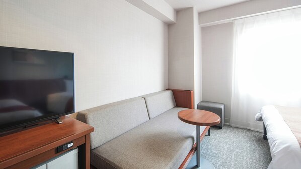 A hotel room with a flat-screen TV, a sofa, a small round table, and a bed.