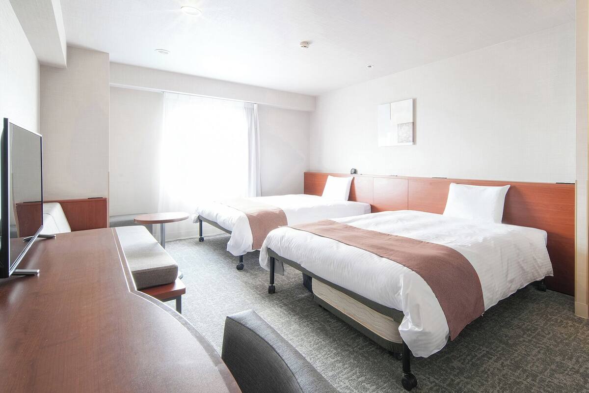 Ett hotellrum med två sängar, ett skrivbord, en stol, en TV och ett stort fönster.