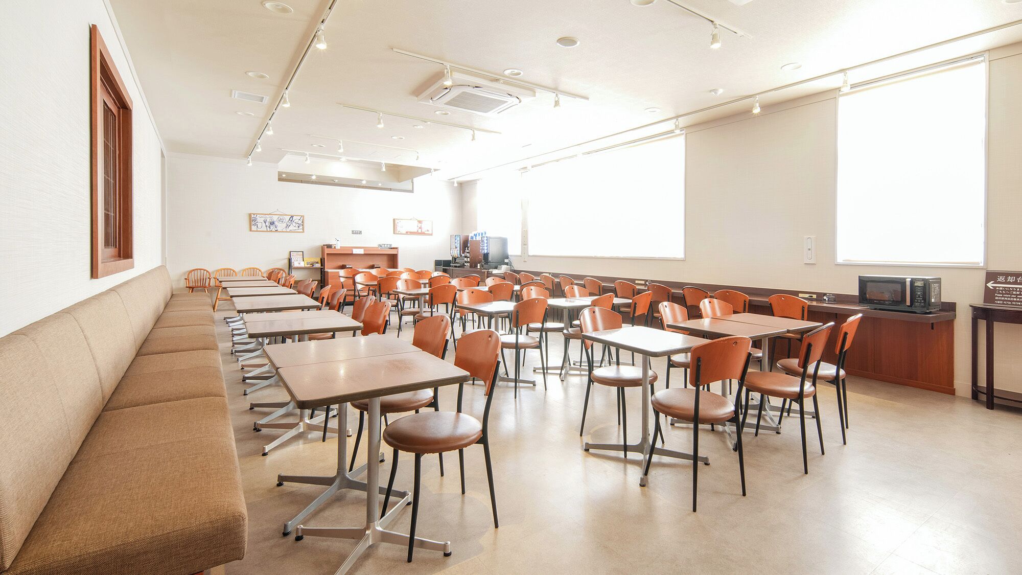 A classroom with rows of desks and chairs, a projector screen, and a television on a desk.