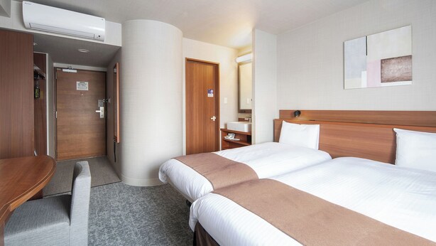 A hotel room with two beds, a wooden headboard, a bedside table, a mirror, and a wall-mounted air conditioner. - Vessel Hotel Miyakonojo (Miyakonojo)