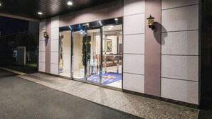 L’entrée d’un hôtel, avec une porte en verre, un comptoir d’accueil à l’intérieur et un tapis bleu qui mène à l’entrée.