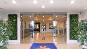 A hotel entrance with a blue carpet featuring a logo, glass doors, and green vertical gardens on either side. - Vessel Hotel Miyakonojo (Miyakonojo)