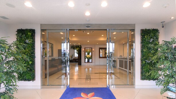 L’entrée d’un hôtel, avec un tapis bleu orné d’un logo, des portes en verre et, de part et d’autre, des jardins verticaux.
