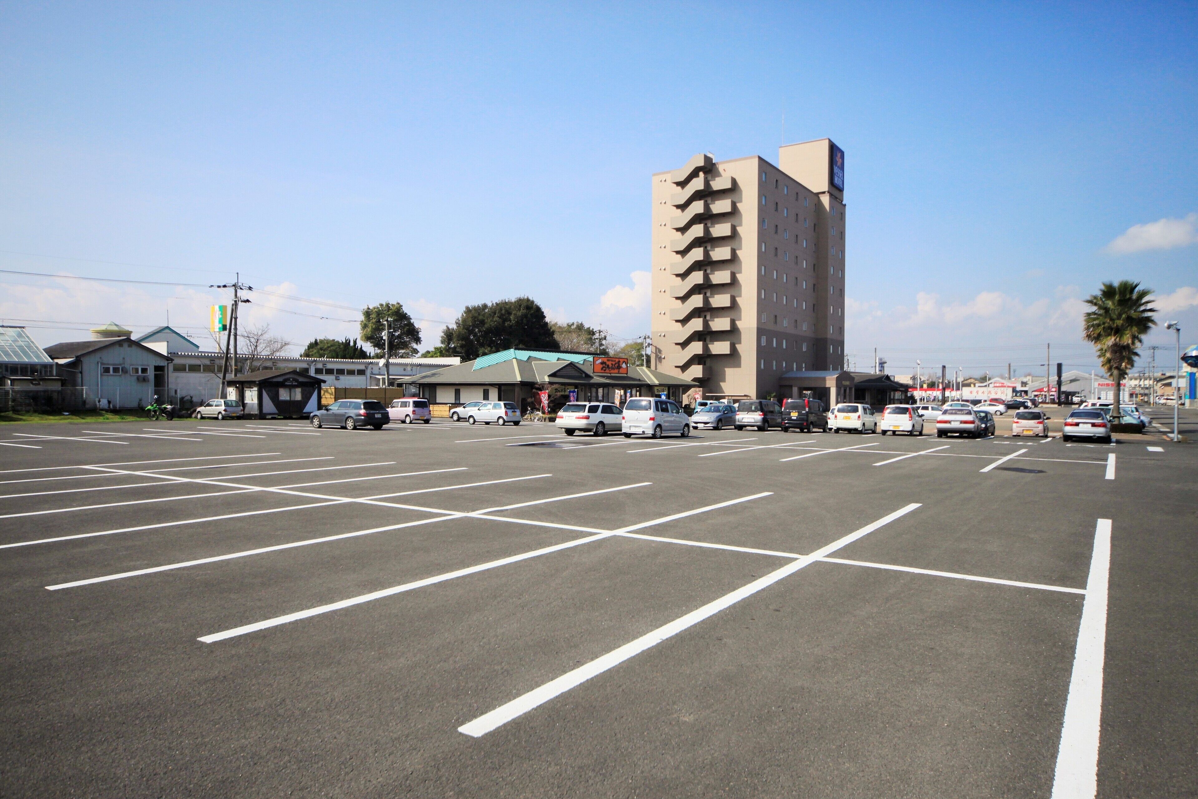Un estacionamiento con varios autos y un alto edificio de hotel al fondo.