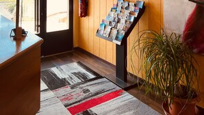 A reception area with a wooden panel wall, a fire extinguisher, a fire exit sign, a magazine rack, and a potted plant. - Hôtel Le Forestia (Pannes)
