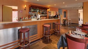 A bar area with stools, a counter with various bottles, and a dining area with a table set for two. - Hôtel Le Forestia (Pannes)