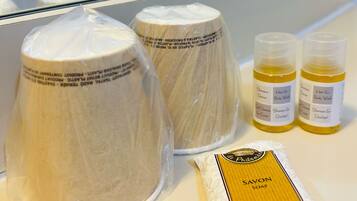 Ein Badezimmer mit einem weißen Waschbecken, zwei Shampooflaschen, einer Seife und einem in Plastik verpackten Handtuch.