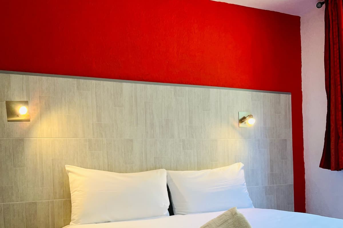A hotel room with a large bed, white bedding, and a red accent wall.