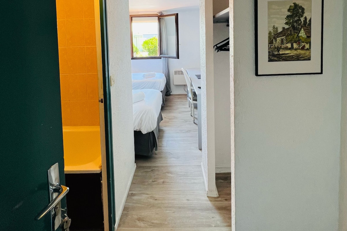 A hallway leading to a bedroom with a bed, a desk, and a framed picture on the wall.