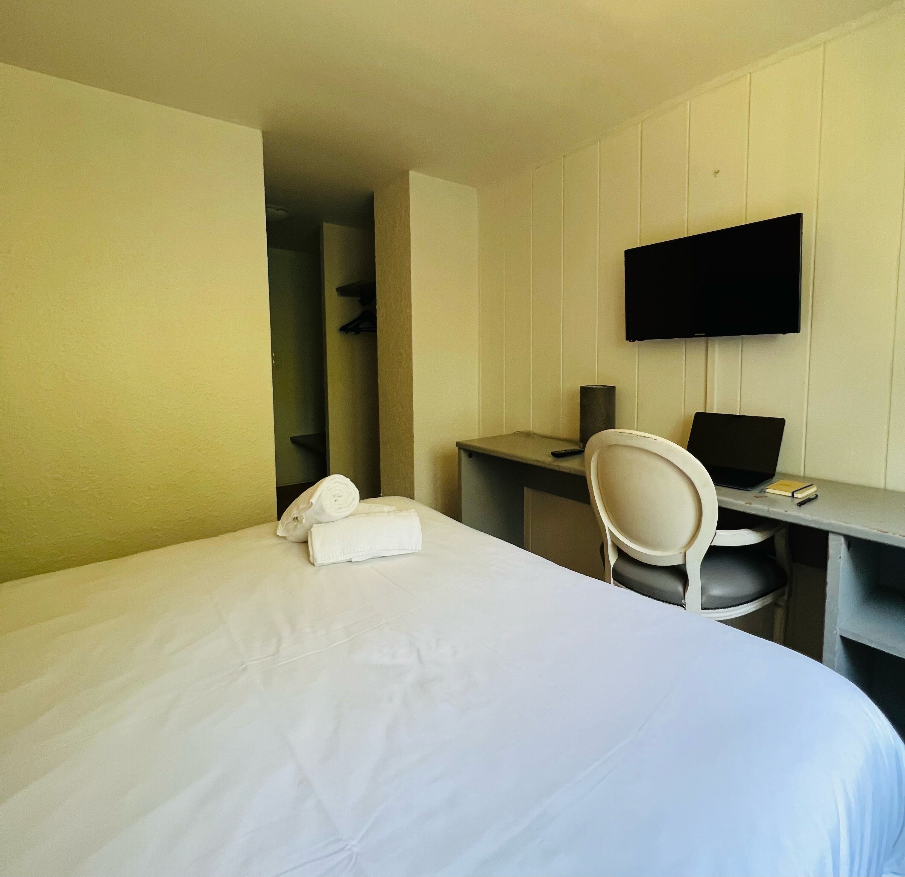 A hotel room with a bed, a desk with a chair, a flat-screen TV, and a telephone.
