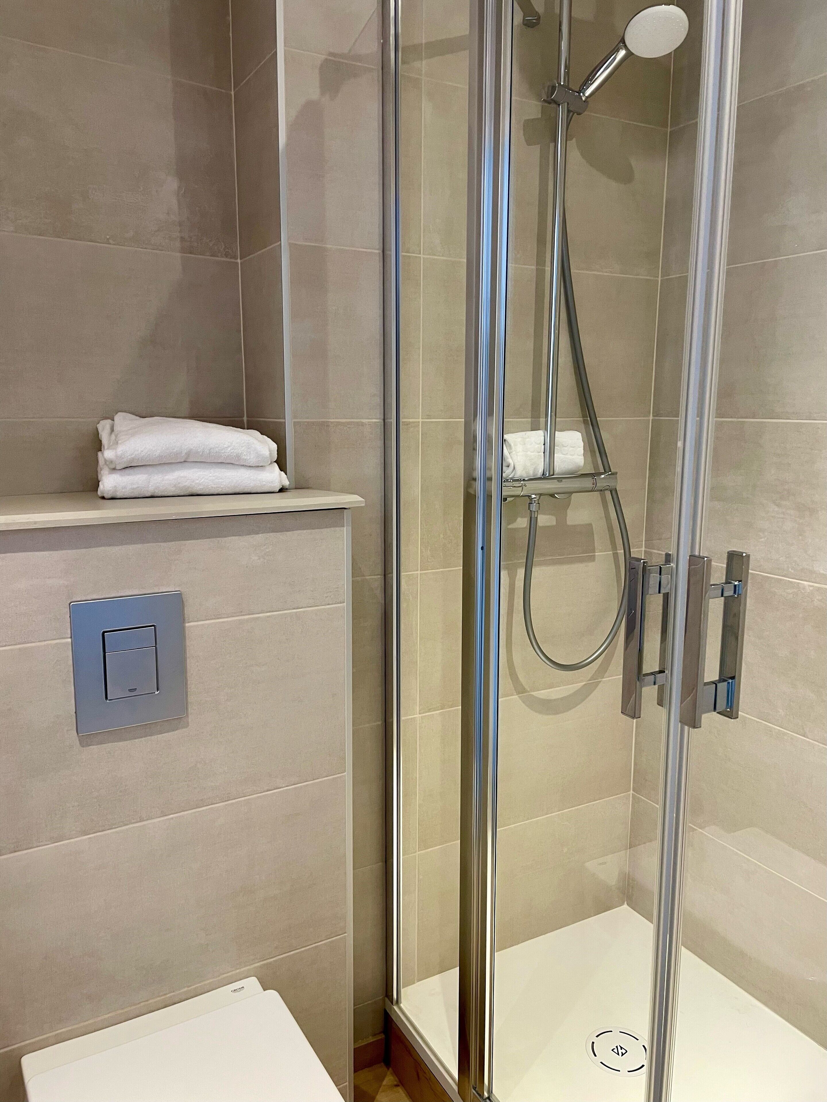 A modern bathroom with a glass-enclosed shower, a towel rack, and a control panel.