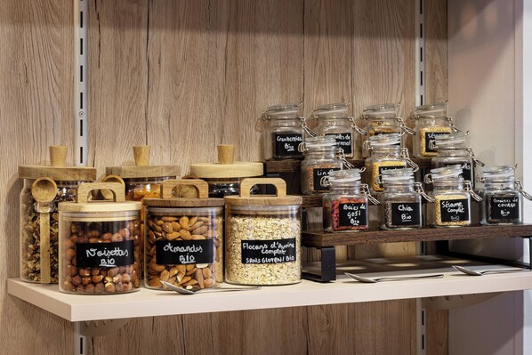 Un estante con diversos alimentos en frascos de vidrio y recipientes de madera, como nueces, granos y especias.