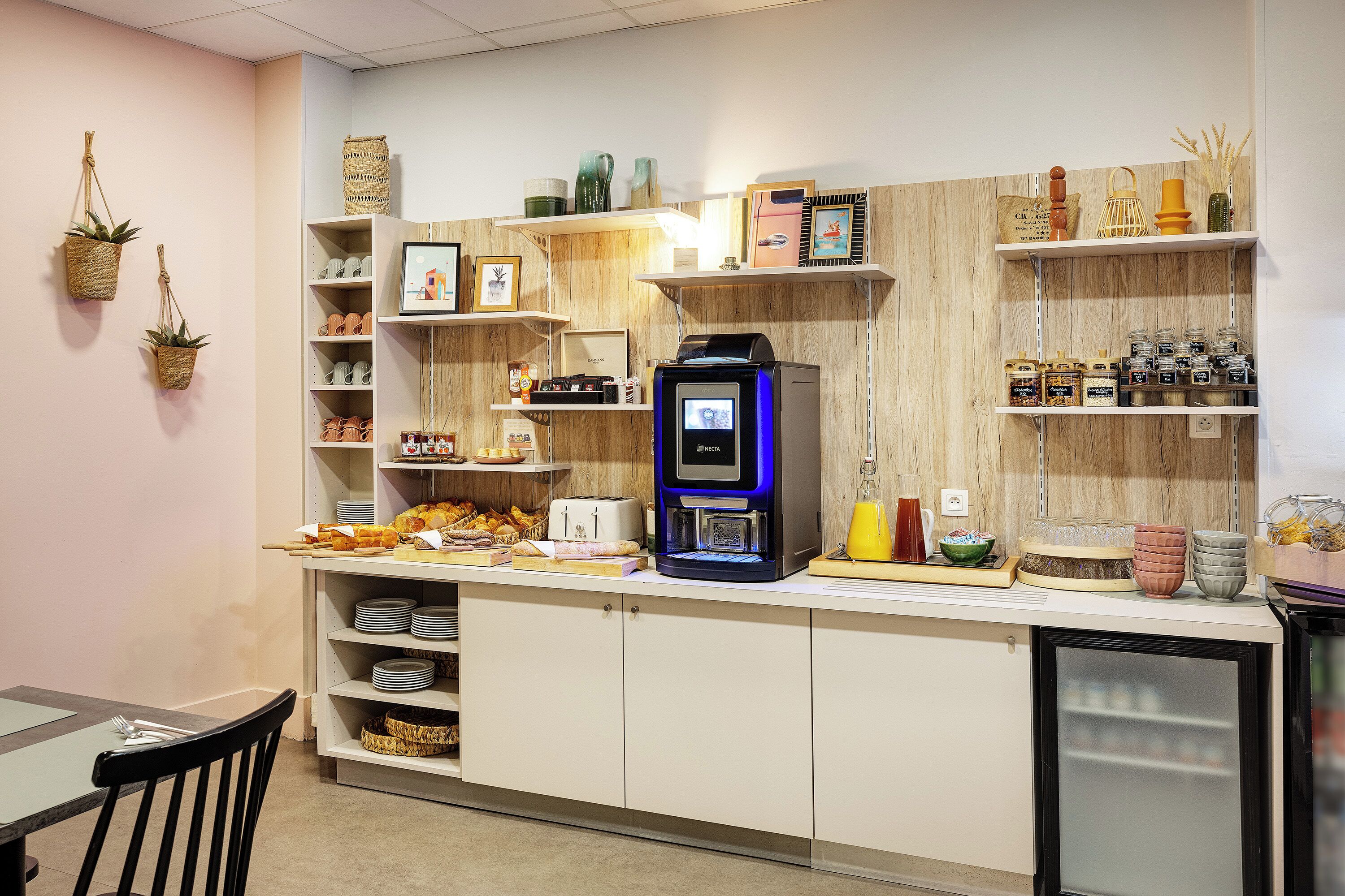 A kitchen area with a coffee machine, shelves with various items, and a refrigerator.