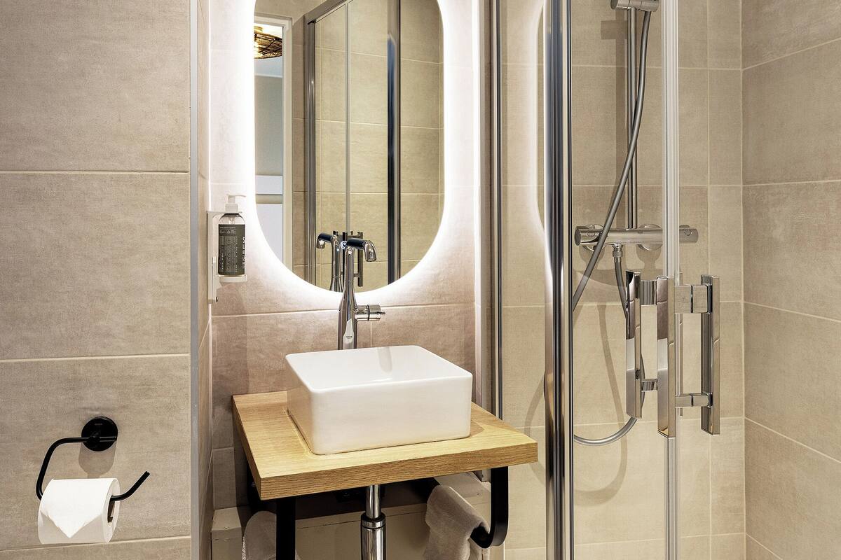 A modern bathroom with a glass-enclosed shower, a rectangular sink, and a round mirror with a light.