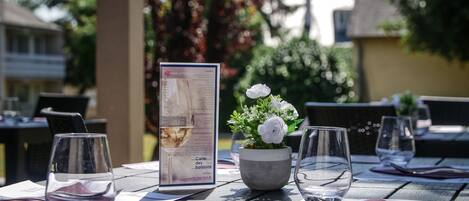 Mesa posta para refeição com menu, planta em vaso com flores brancas e copos de vinho vazios.
