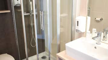 Et moderne badeværelse med en bruseniche med glasvægge, en hvid vask og et toilet.