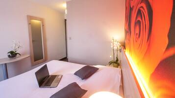 A hotel room with a bed, a laptop, a mirror, and a large floral painting on the wall.
