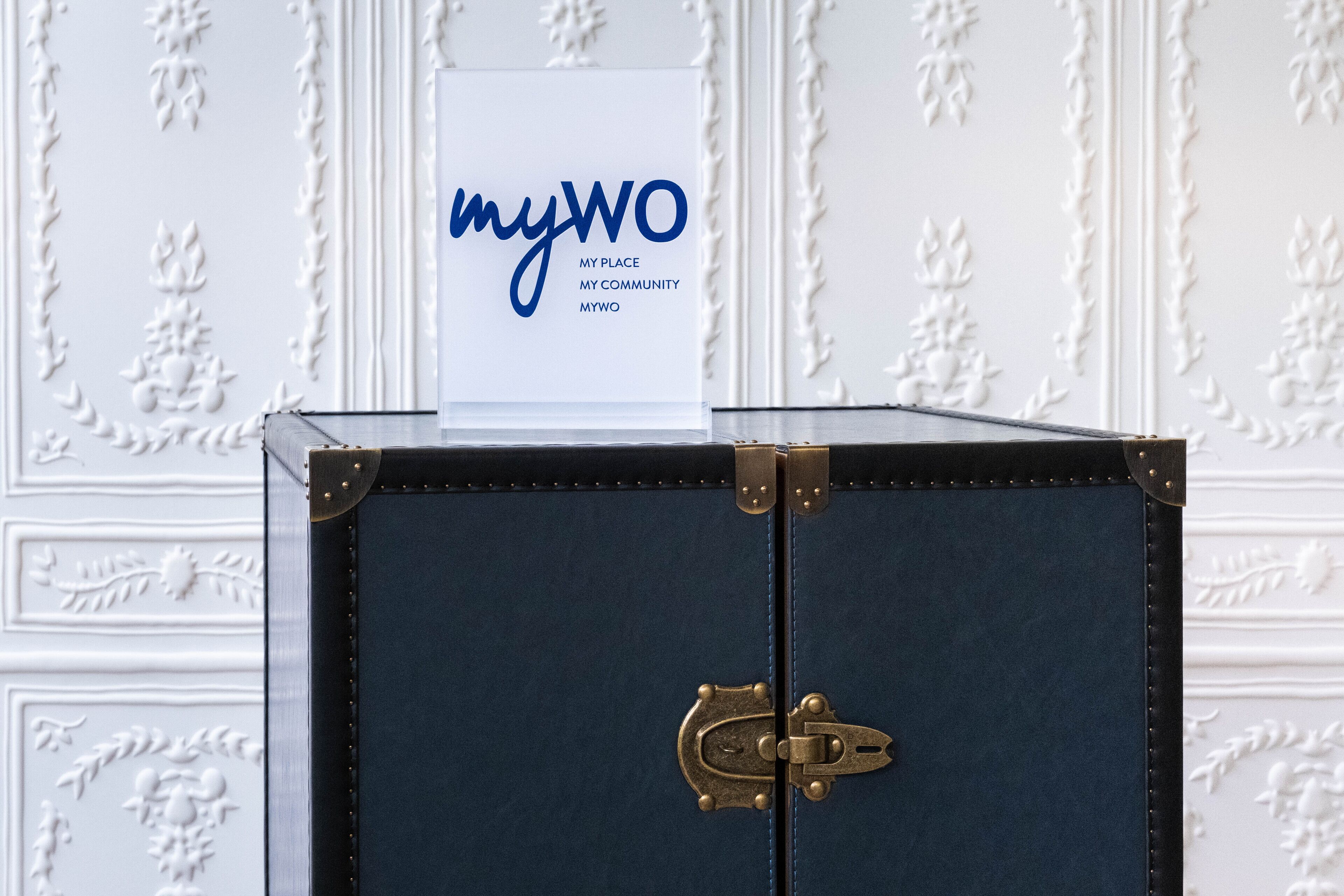 Une valise bleu foncé avec un fermoir en laiton et une étiquette blanche sur laquelle est inscrit : « myWO, mon chez-moi, ma communauté, myWO ».