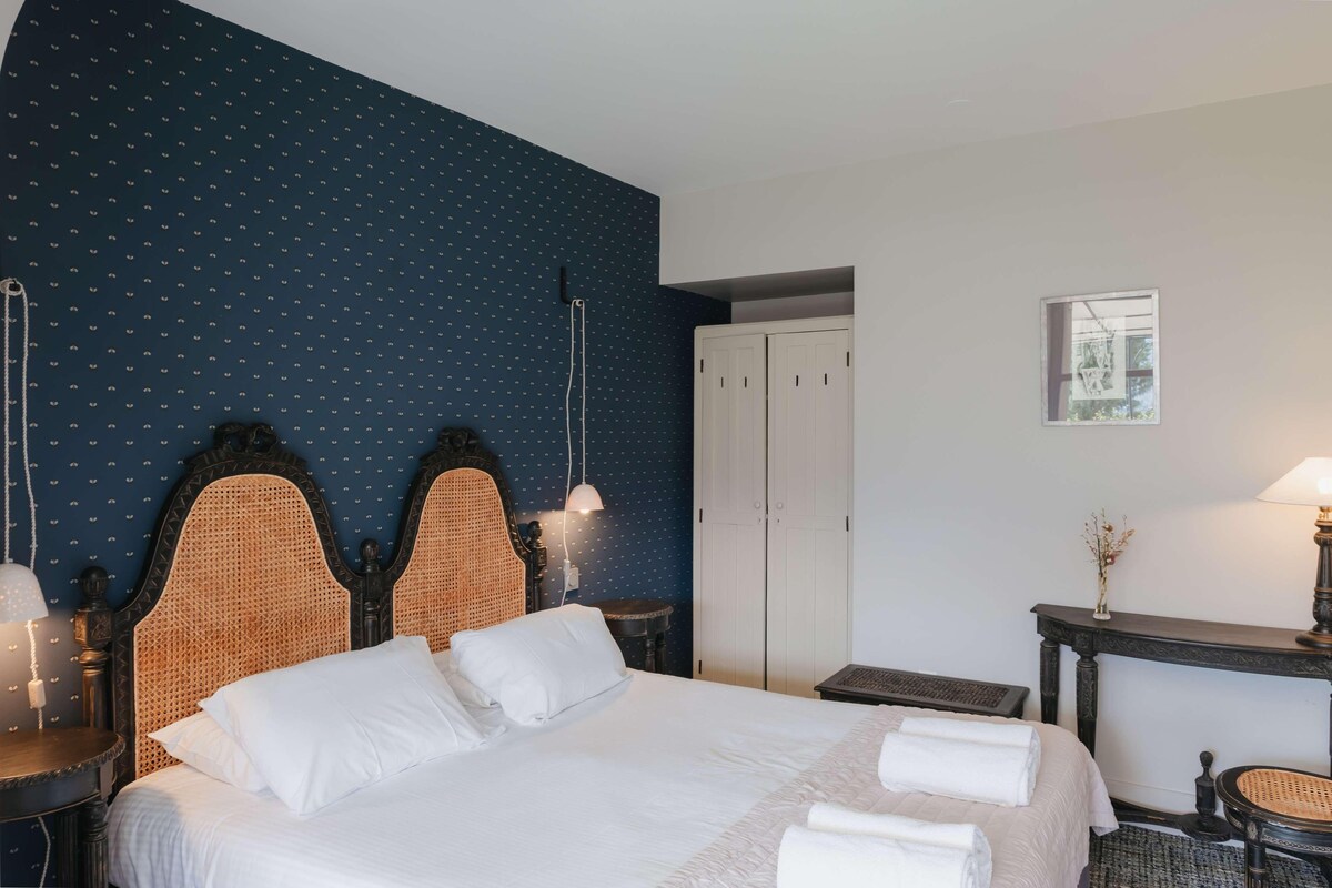 Une chambre d’hôtel avec un grand lit, une armoire, une petite table et une lampe fixée au mur.