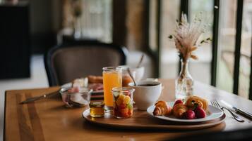 Una mesa de desayuno con cruasanes, fresas, un vaso de jugo de naranja, un tazón de cereal y un frasco pequeño de mermelada.