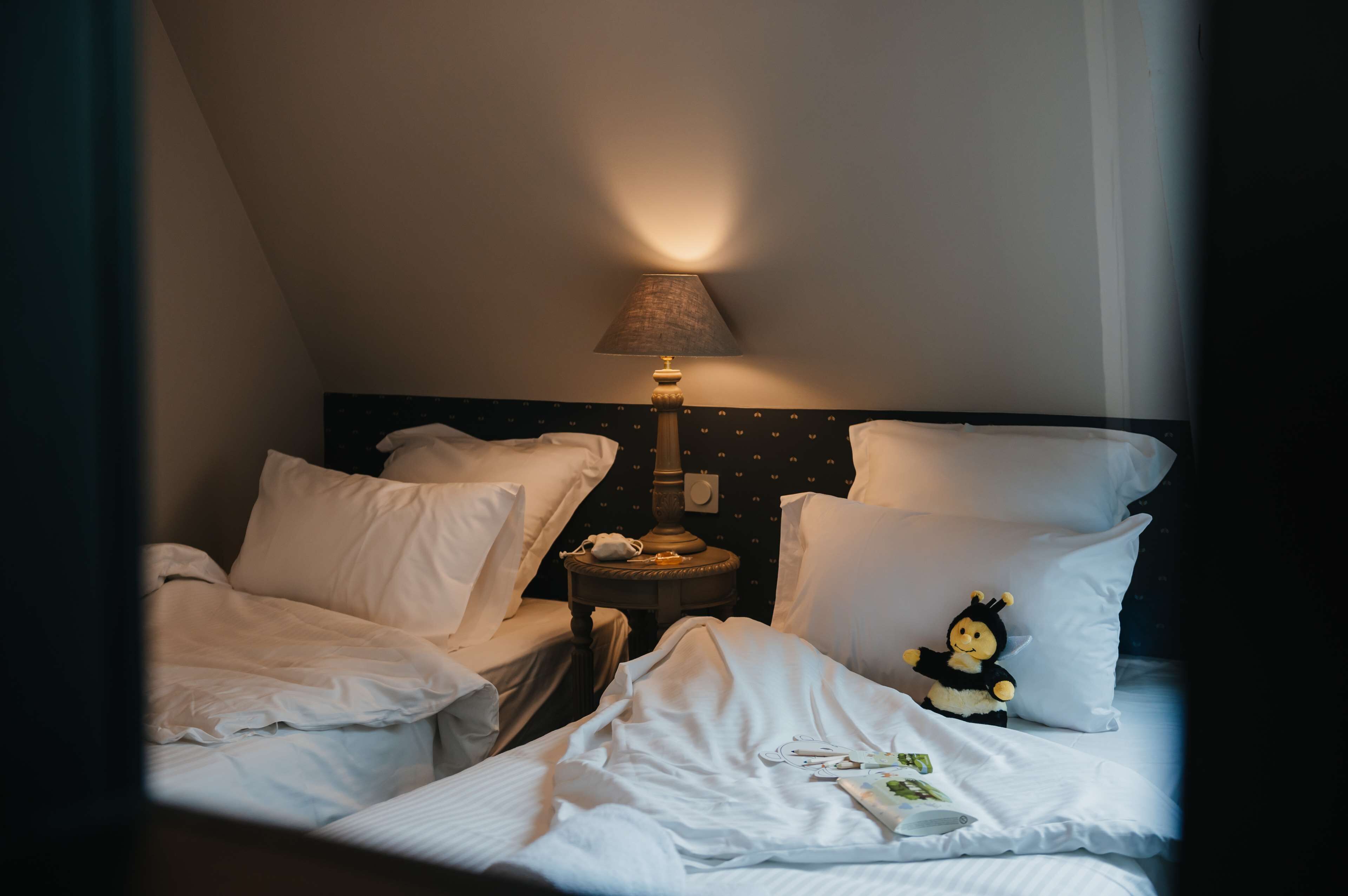 Hotellihuone, jossa on kaksi sänkyä, yöpöytä, lamppu ja pieni koriste-esine.