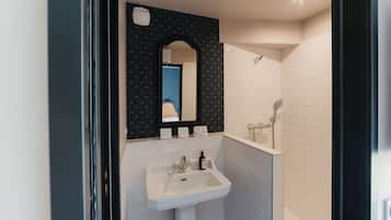 Un baño con lavamanos blanco, espejo y ducha.