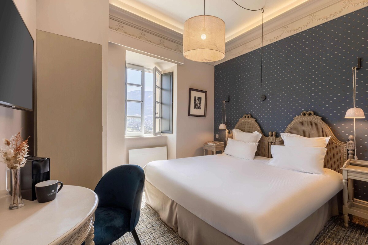 A hotel room with a large bed, a desk with a chair, a coffee maker, and a window with a view.