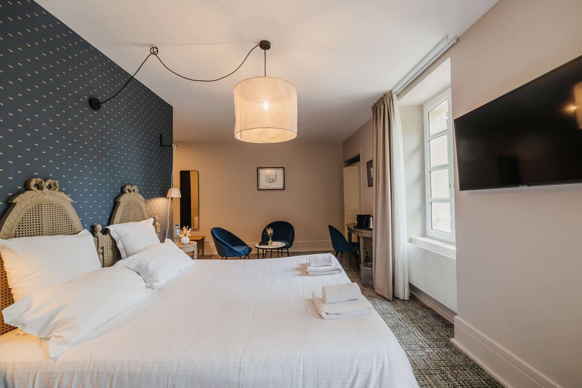 Une chambre d’hôtel avec un grand lit, un bureau avec une chaise, une télévision et une fenêtre avec des rideaux.