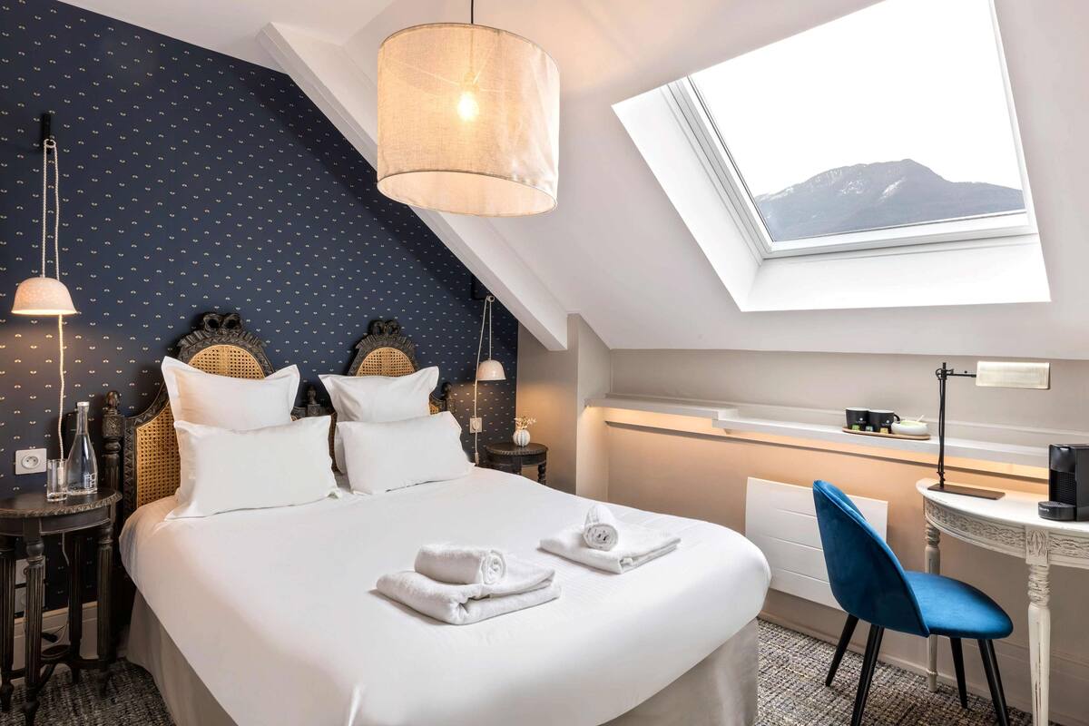 Une chambre d’hôtel avec un grand lit, un bureau avec une chaise, une fenêtre donnant sur la montagne et un luminaire au plafond.