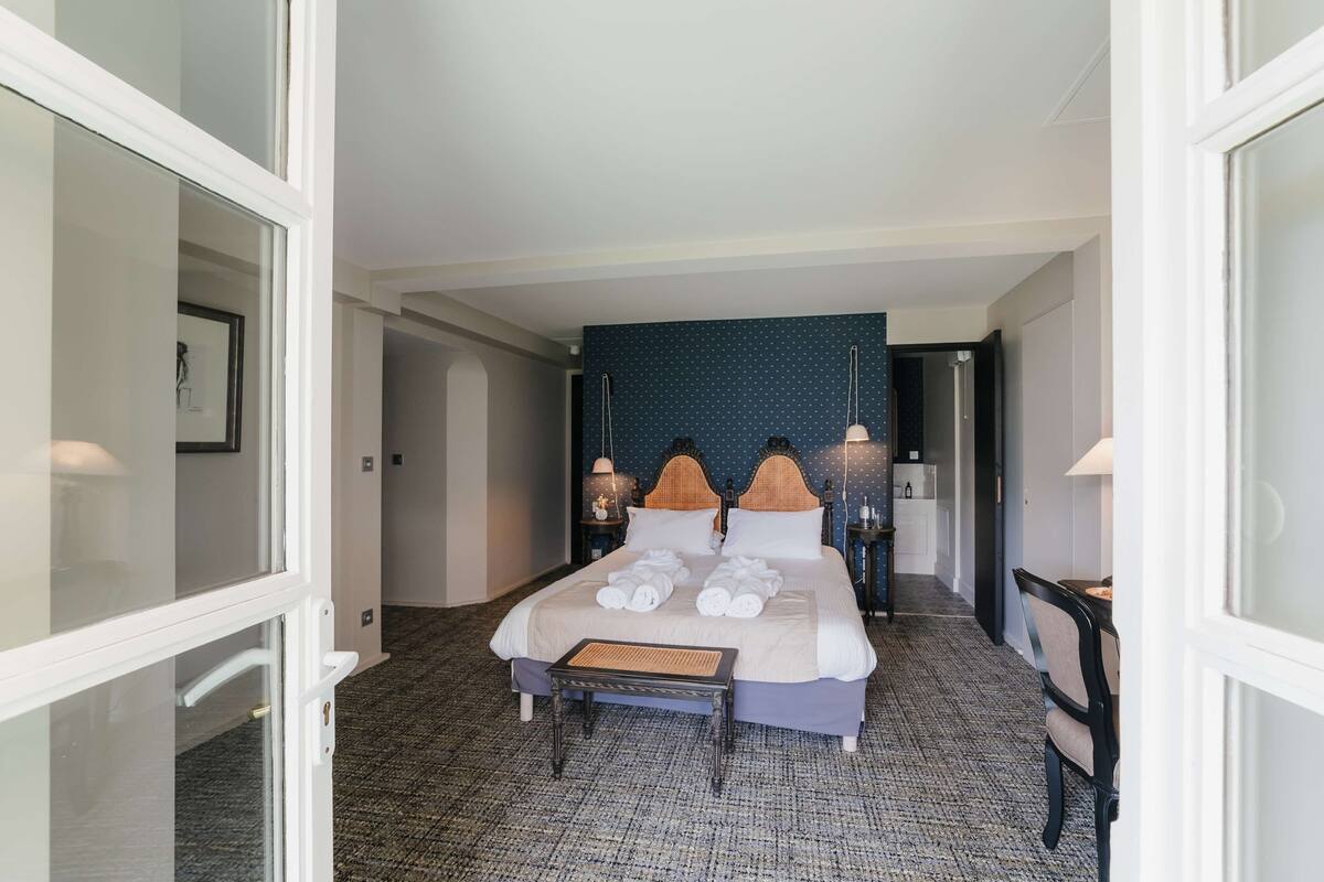 Une chambre d’hôtel avec un grand lit, deux tables de chevet avec des lampes, une petite table avec des serviettes et une chaise.