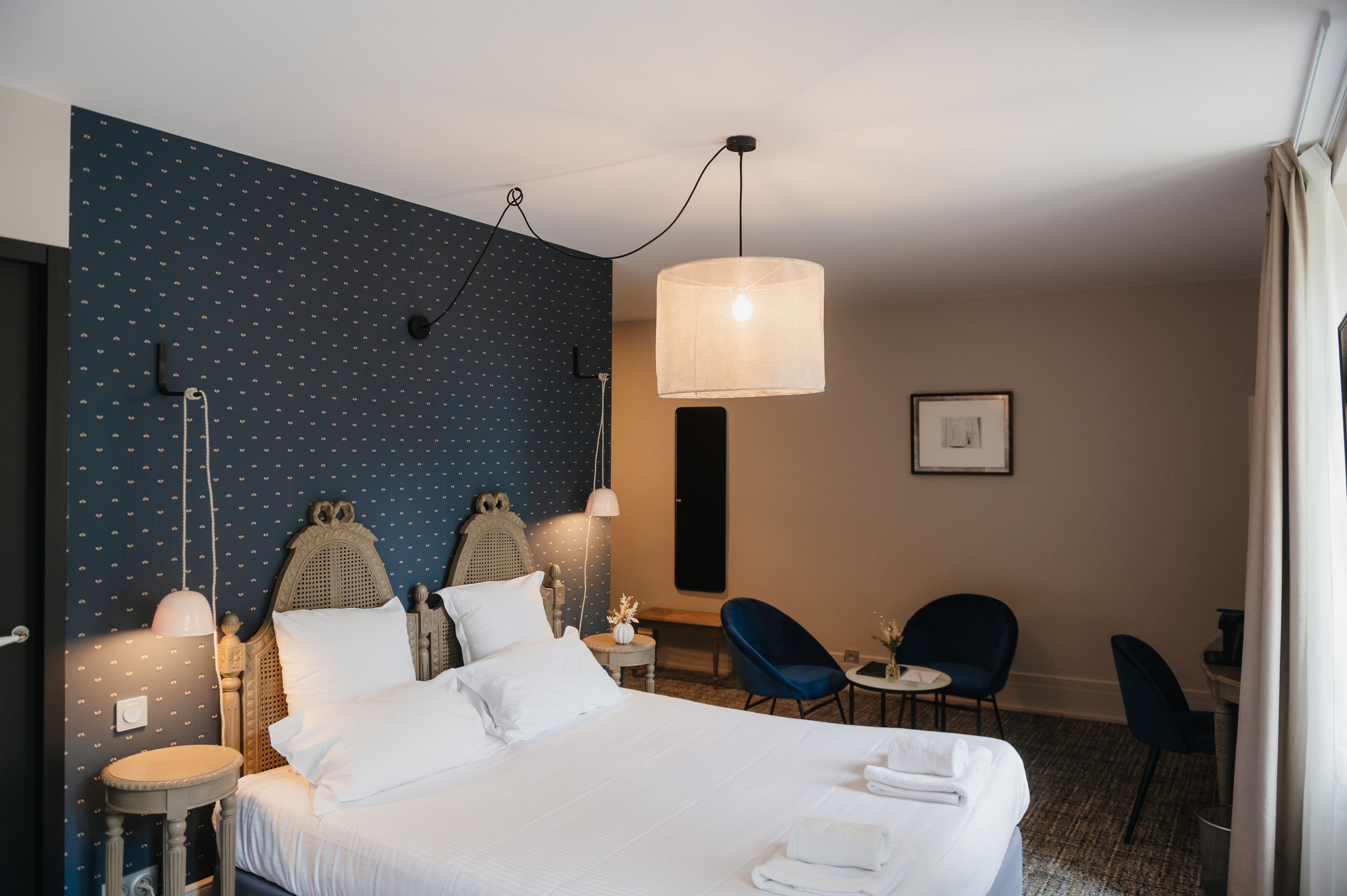 Habitación de hotel con cama, dos sillas, una mesita, una lámpara y una pared con estampado de lunares.