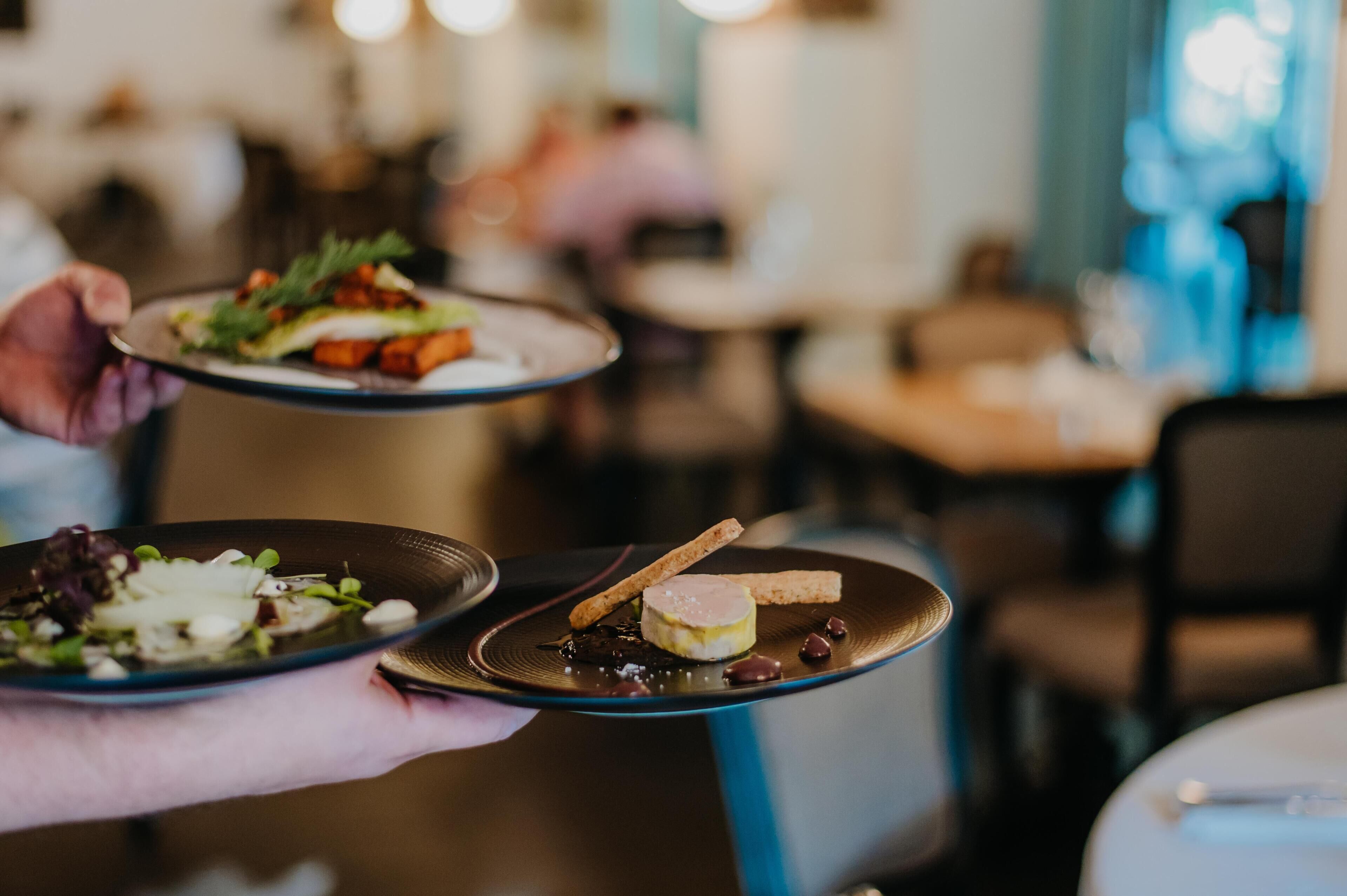 Eine Person hält zwei Teller mit Essen in einem Restaurant.