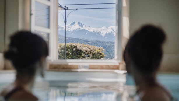 Two people in a swimming pool with a view of snow-capped mountains through a window. - Hotel La Robeyere, BW Signature Collection (Embrun)