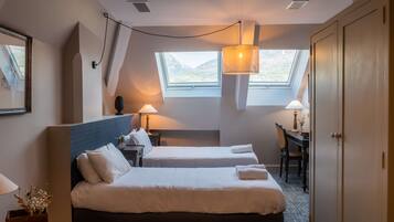 Une chambre d’hôtel avec deux lits, un bureau et une chaise. Elle est dotée de fenêtres de toit et d’un ventilateur de plafond.
