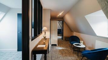 Une chambre d’hôtel moderne avec un plafond en pente, un petit coin repas, une chaise bleue et une lampe.