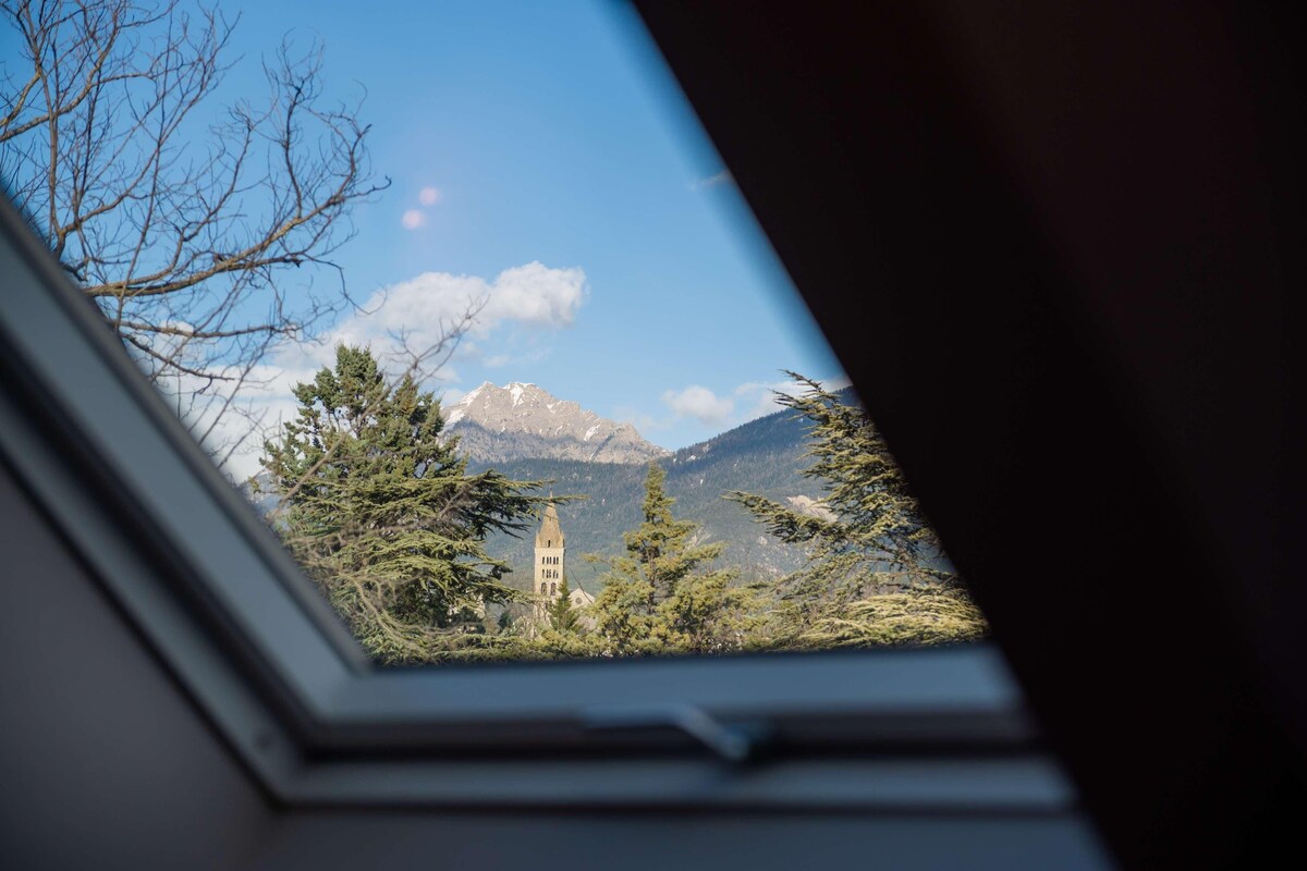 A view through a skylight of a mountain landscape with a church tower.