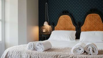A neatly made bed with rolled white towels, a dark blue polka dot wall, and a hanging lamp.