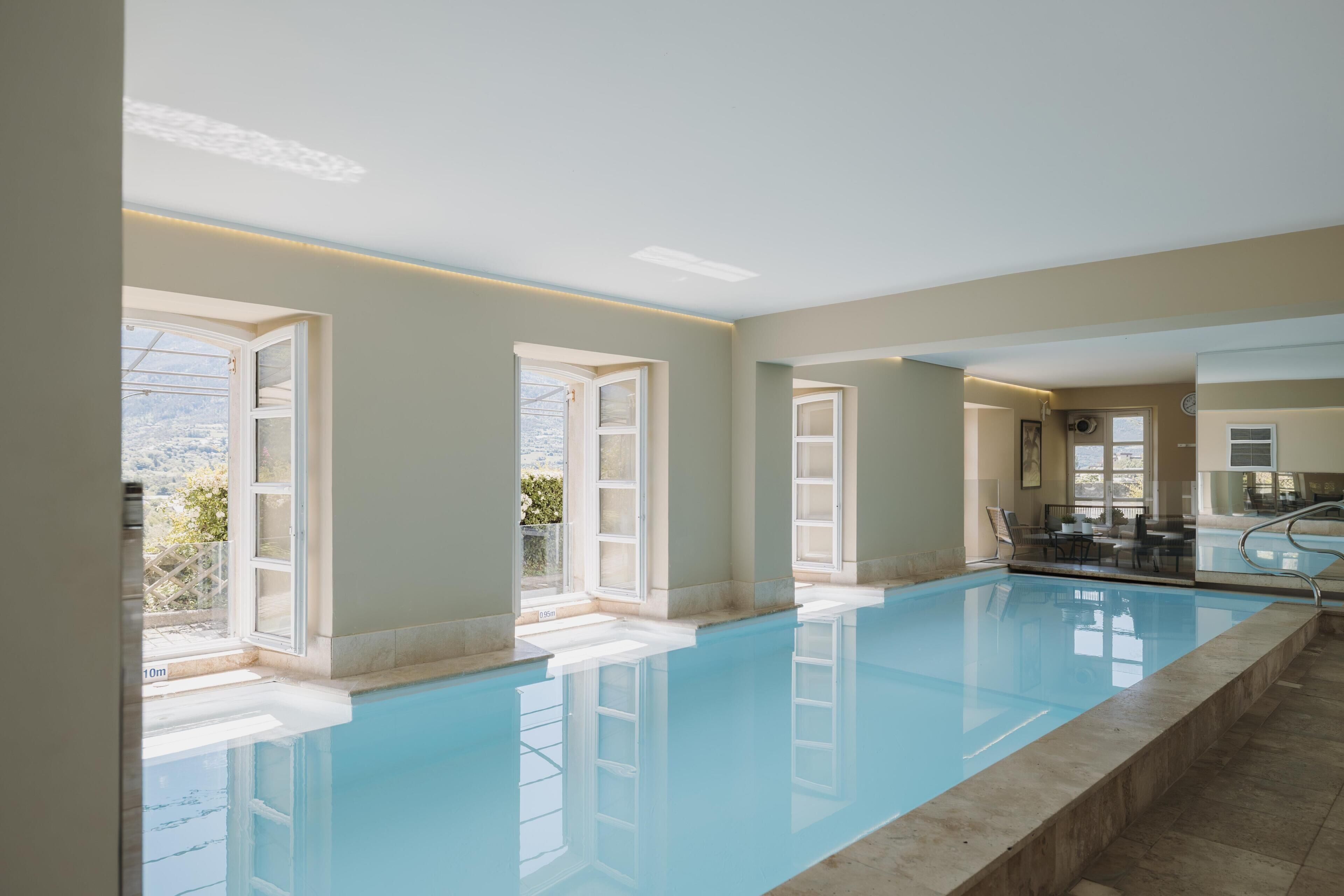 A swimming pool with clear blue water, large windows, and a view of the outdoors.