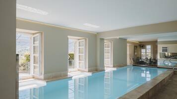 A swimming pool with clear blue water, large windows, and a view of the outdoors.