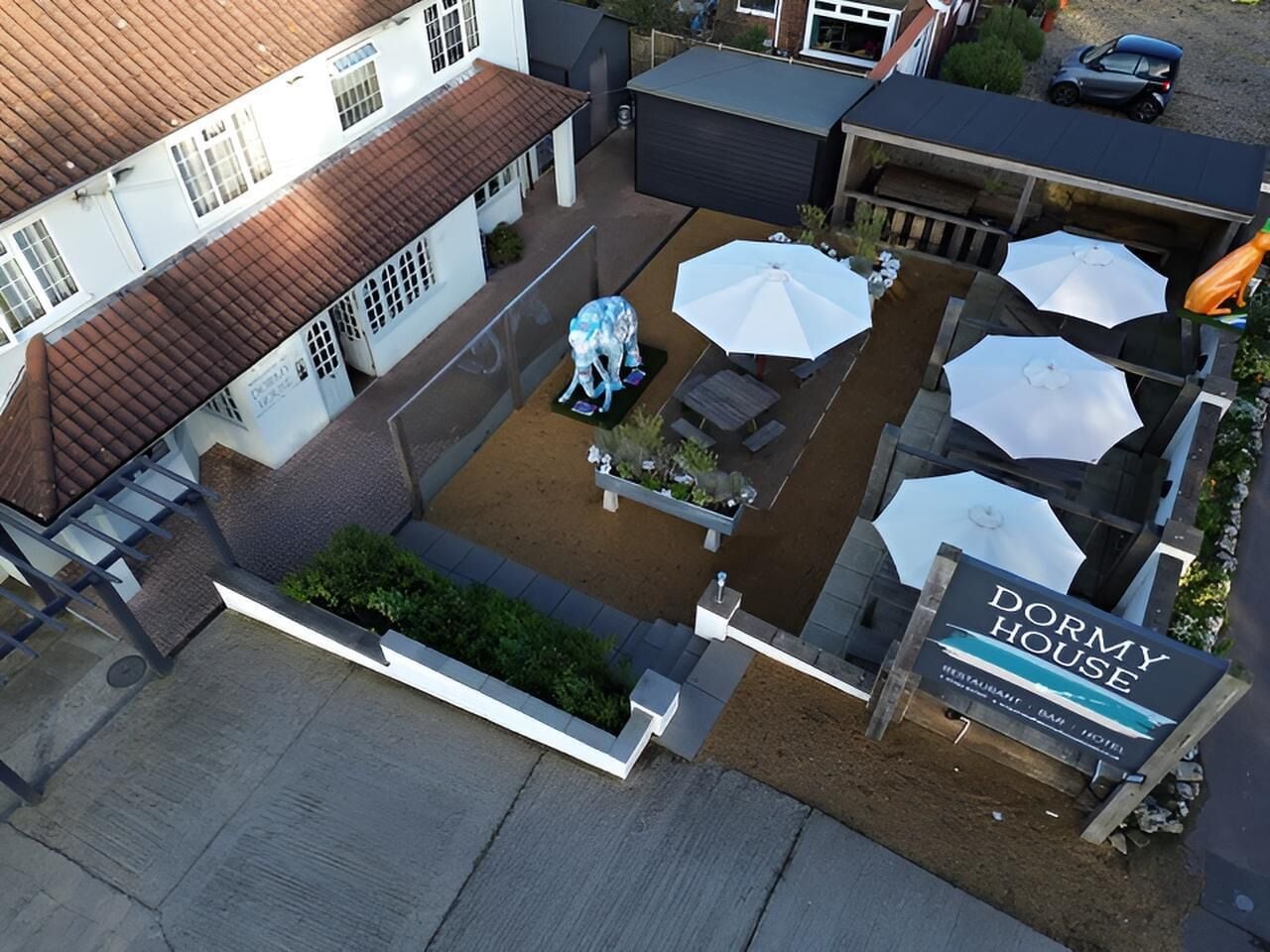 A courtyard with outdoor seating, umbrellas, and a sign for 'DORMY HOUSE' hotel.