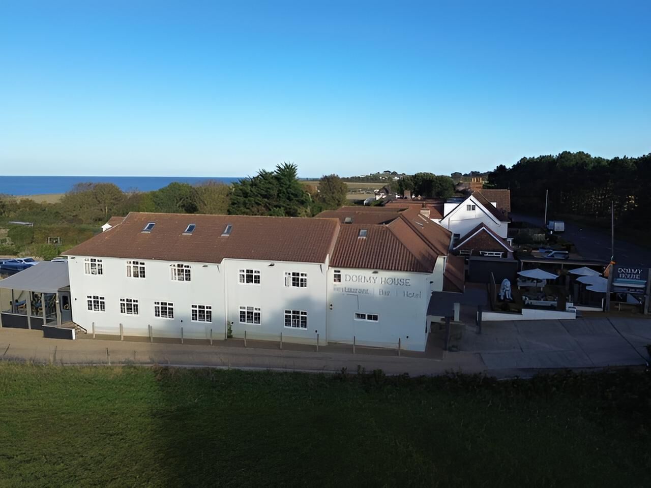 Ein weißes Gebäude mit braunem Dach, mit der Aufschrift 'DORMY HOUSE', mit Blick auf das Meer im Hintergrund.